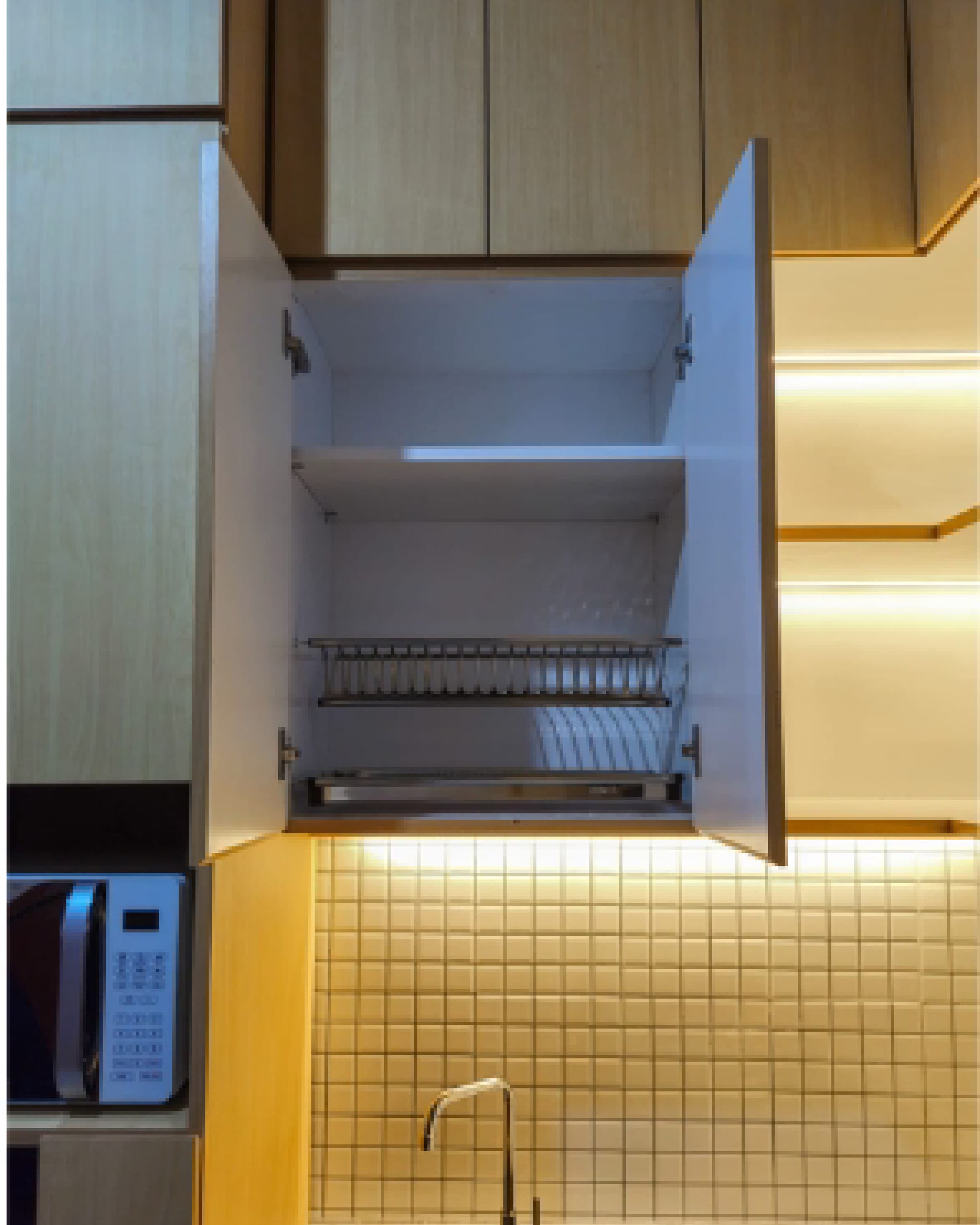 Site documentation of an open overhead cabinet with a built-in plate rack and warm under-cabinet lighting.
