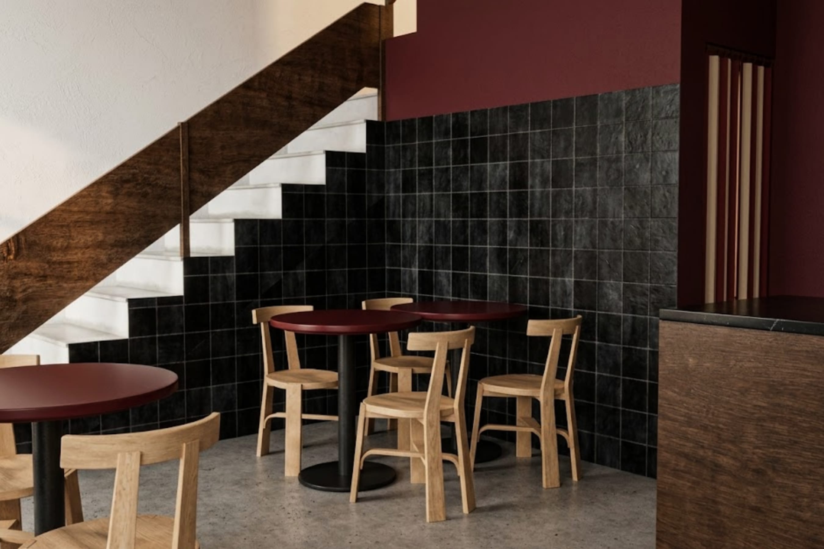 Tables tucked under the stair, against a black tiled wall and a white stringer.