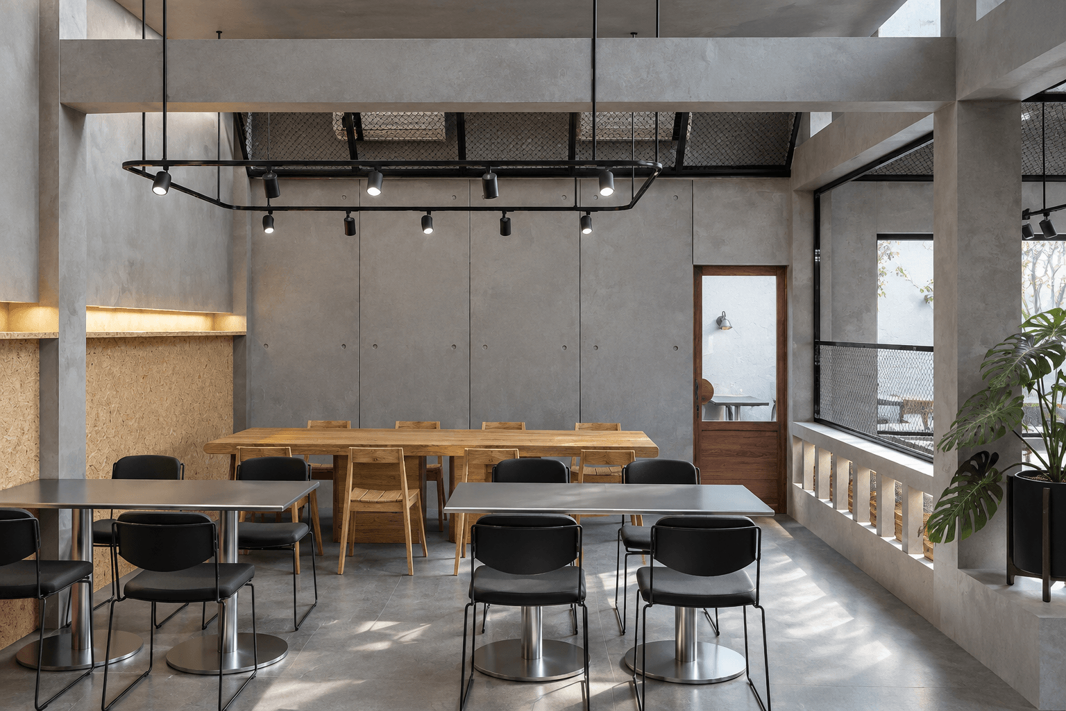 A long timber table and rows of black chairs under the track-light frame.