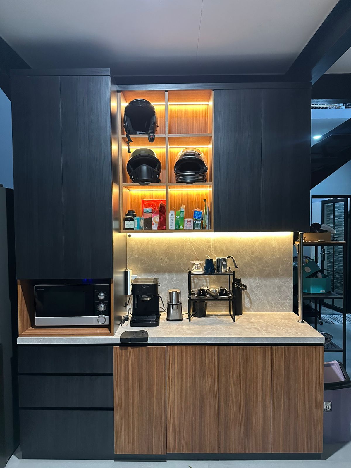 Dark timber-grain cabinetry with warm-lit open shelving and a stone-look counter.