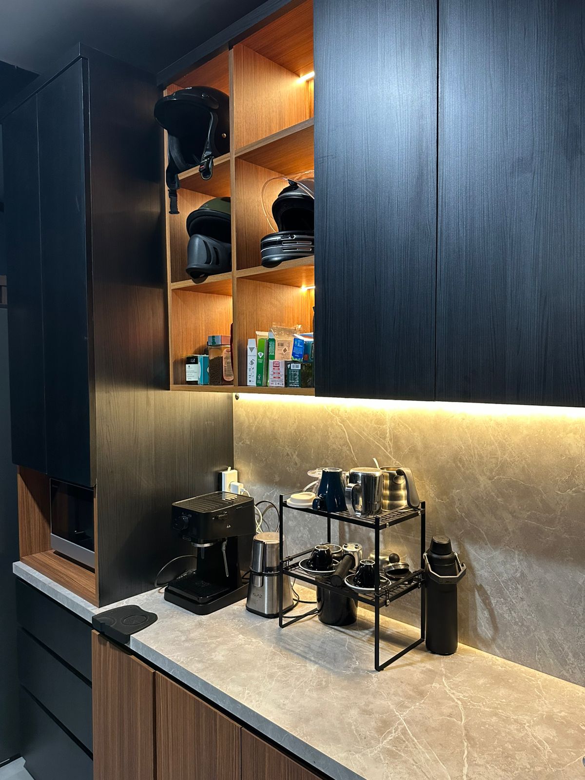 A coffee station on a stone-look counter, beneath the lit shelving.