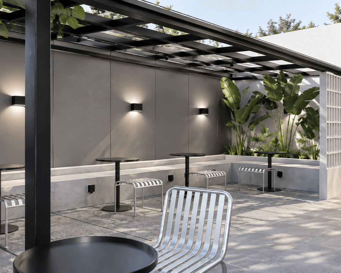 Covered terrace with a slatted roof, wall lights, planting and metal chairs.