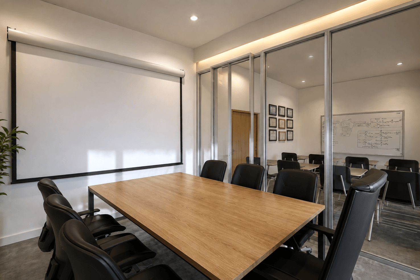 Meeting room with a timber table, black chairs, a projection screen and glazed partitions.