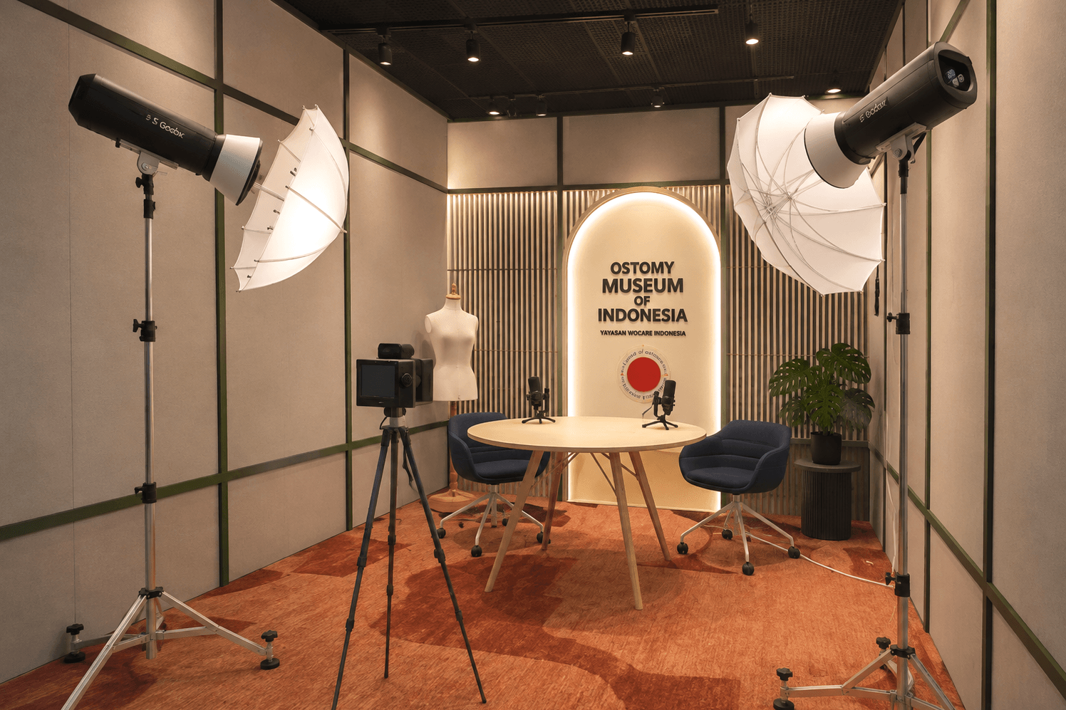 Recording studio with a round table, microphones, lighting umbrellas and an illuminated museum sign.