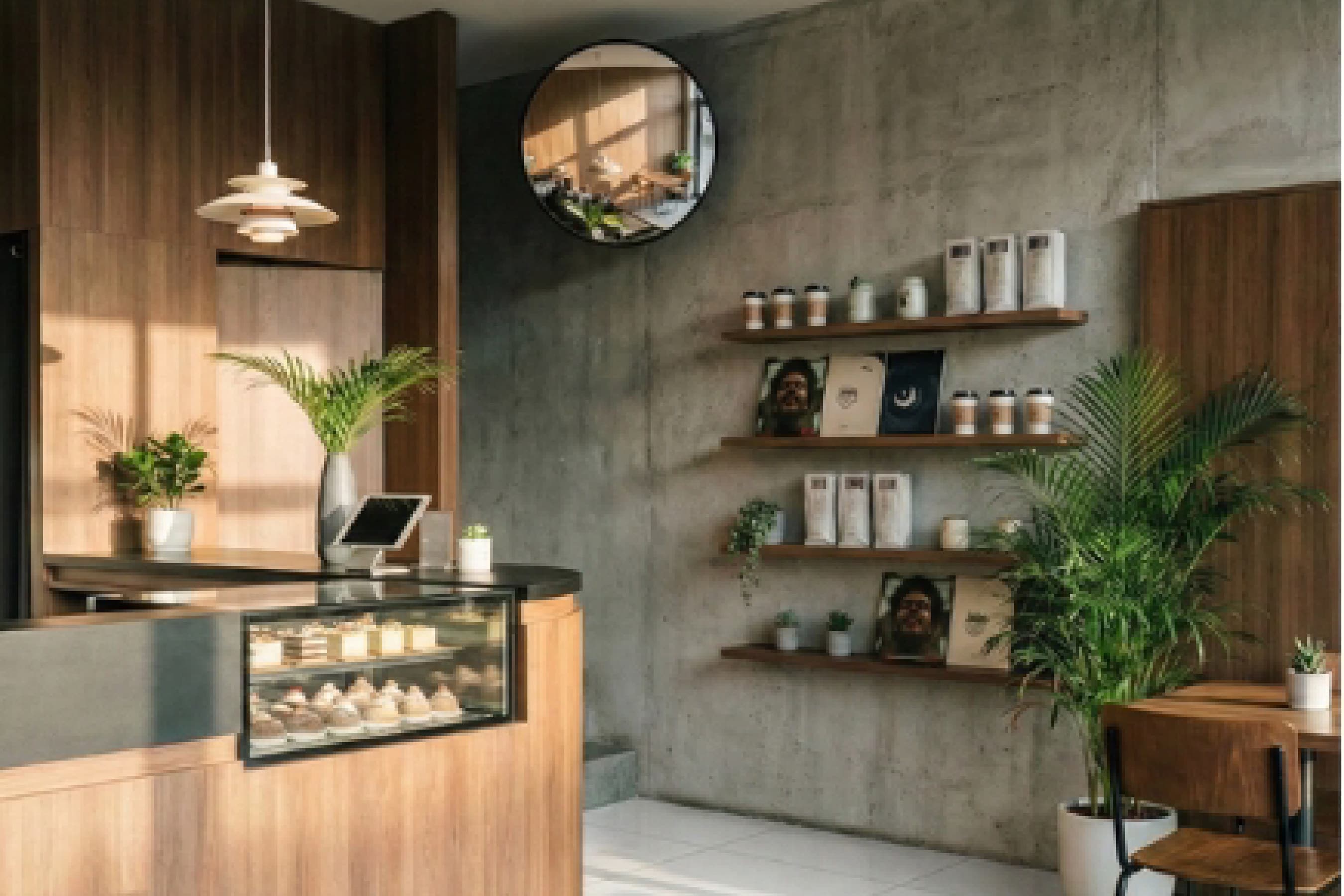 Pastry counter with open timber shelving, ceramic cups and a round mirror on the wall behind.