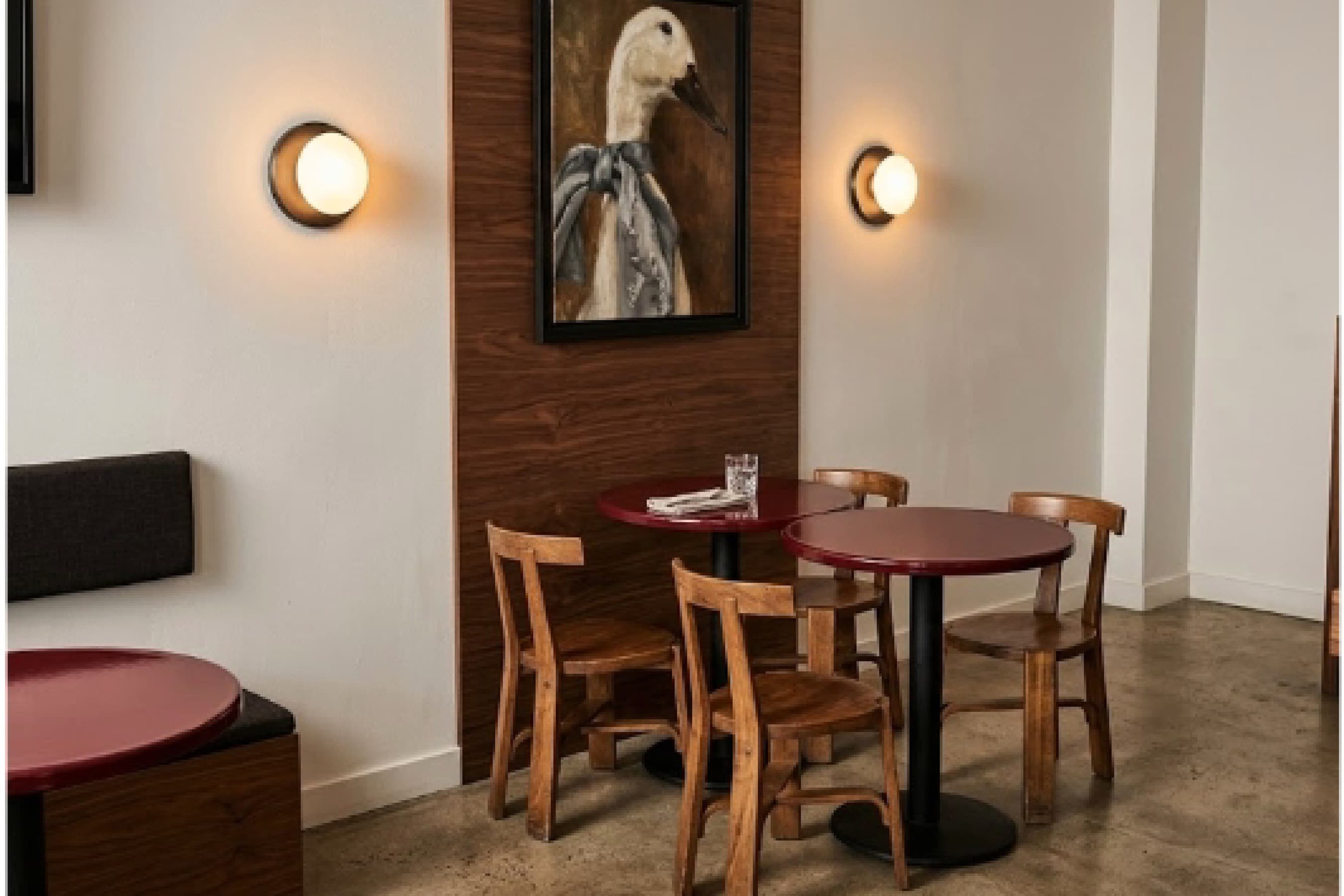 Seating nook with a round red table, wall sconces and framed artwork above a banquette.