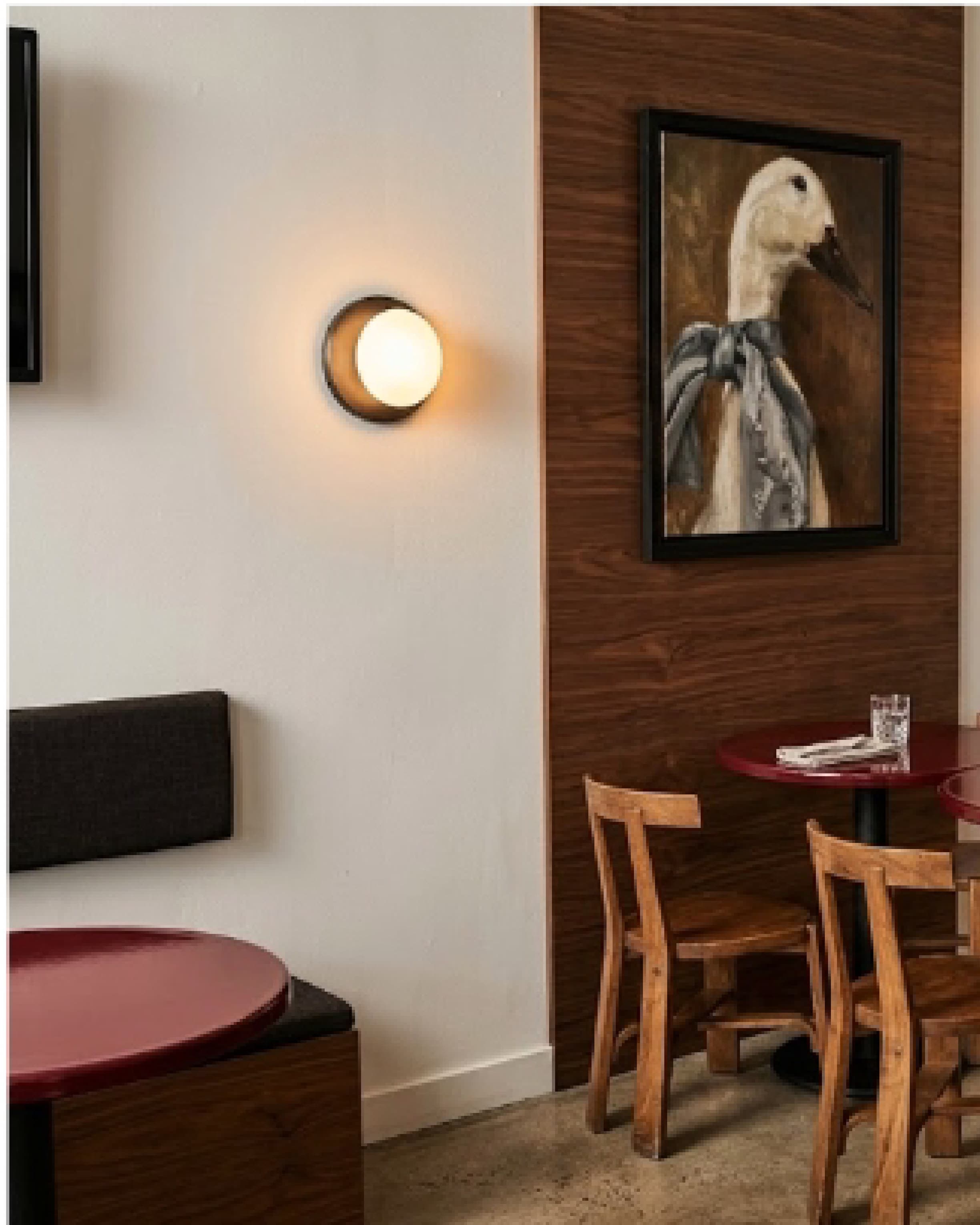 Seating nook with a round red table, wall sconces and framed artwork above a banquette.